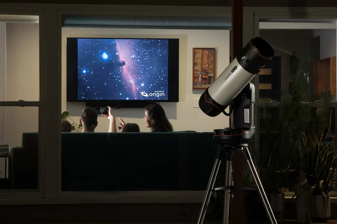 The Origin on its tripod in a dark room, in front of a large screen showing a nebula to a seated audience.